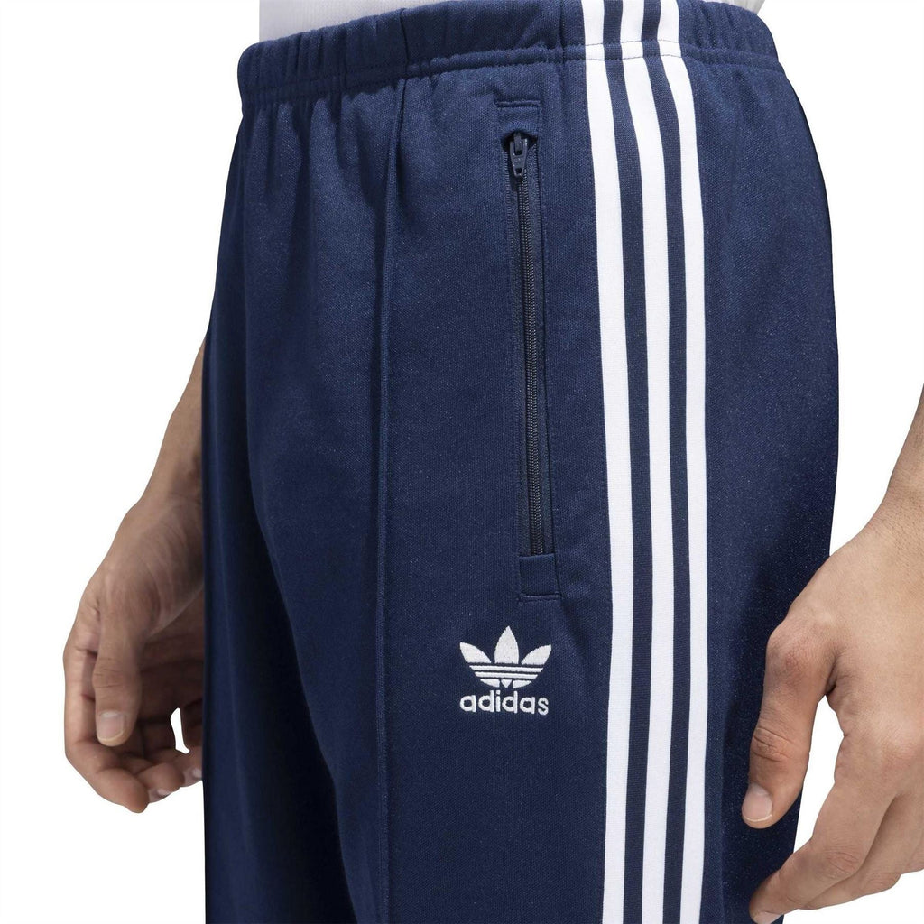 adidas track pants close-up: navy elastic waist, zip pocket, trefoil logo, white stripes