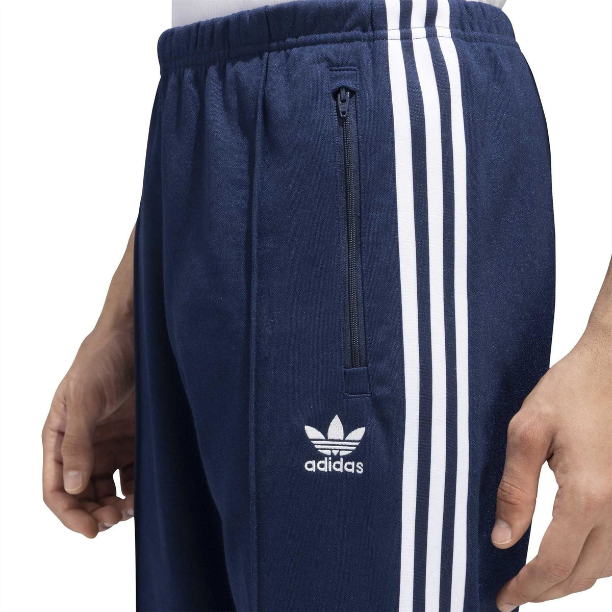 adidas track pants close-up: navy elastic waist, zip pocket, trefoil logo, white stripes