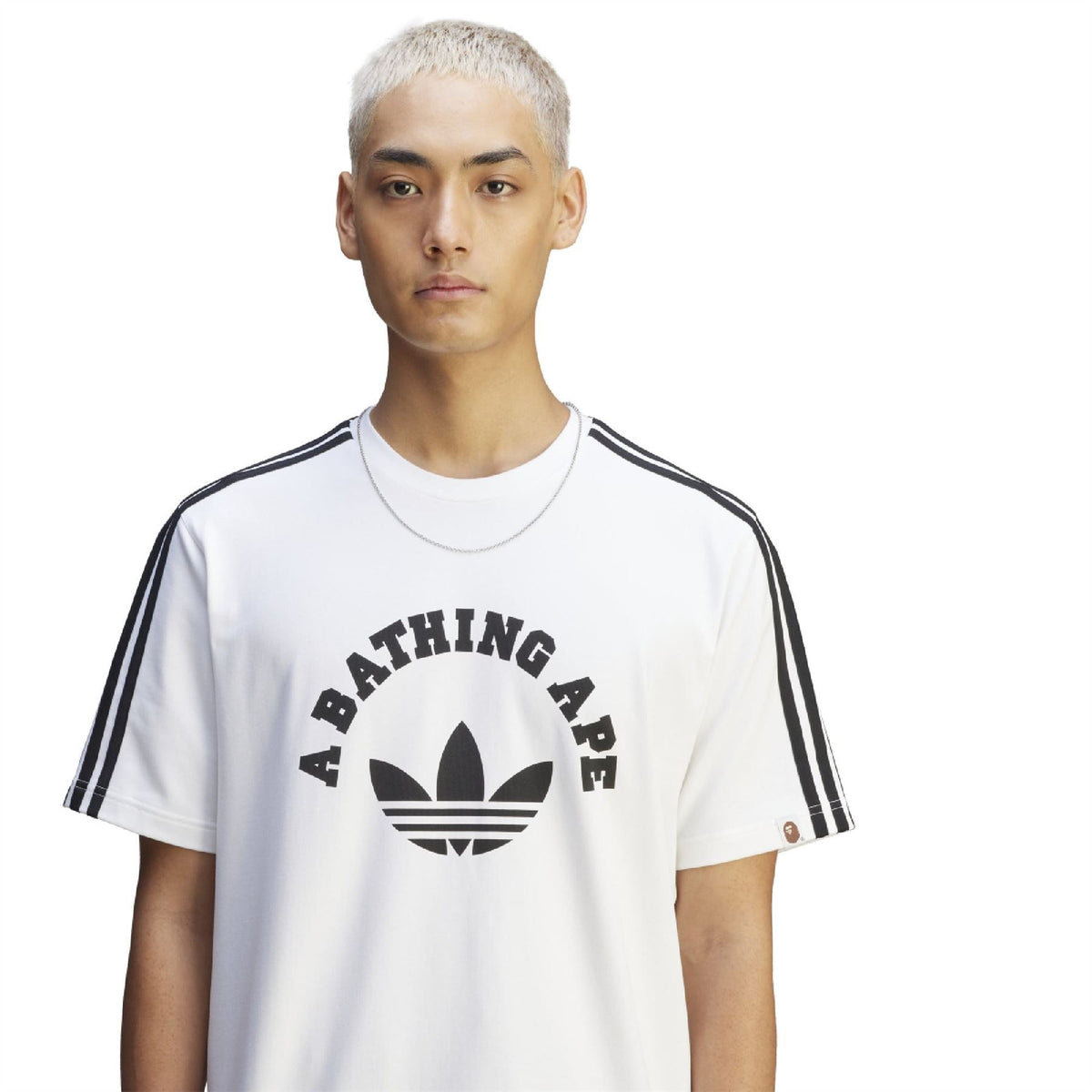 White T-shirt on model: A BATHING APE graphic front and black adidas-style shoulder stripes