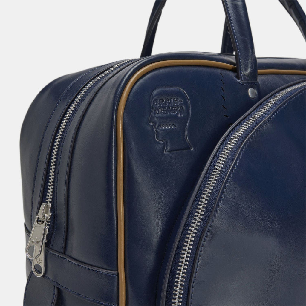 Navy duffel bag close-up showing front pocket zipper and embossed face logo patch.