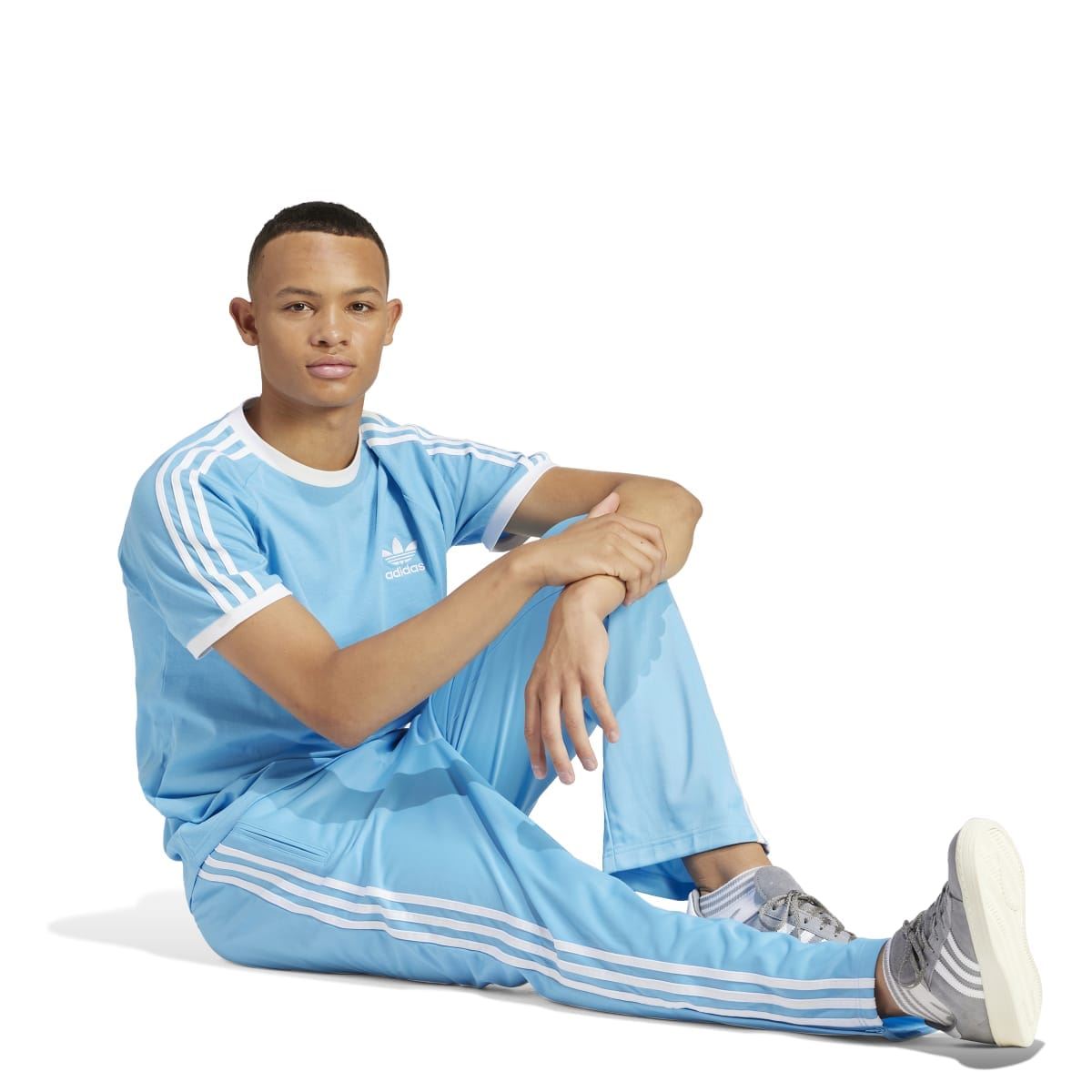 Light blue adidas T-shirt with three white stripes on sleeves, seated model pose