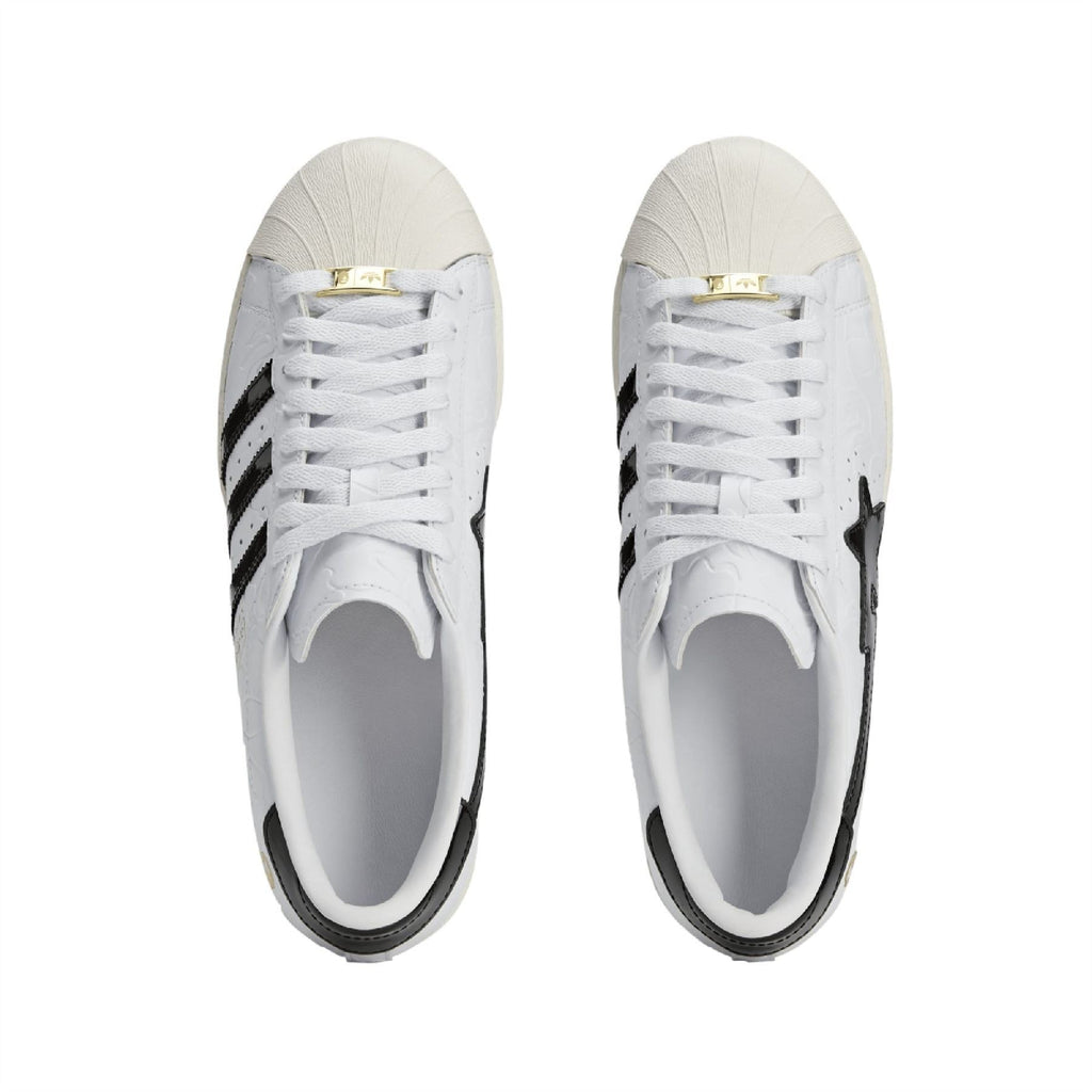 Pair of white sneakers with white laces, black side stripes, and gold lace tag
