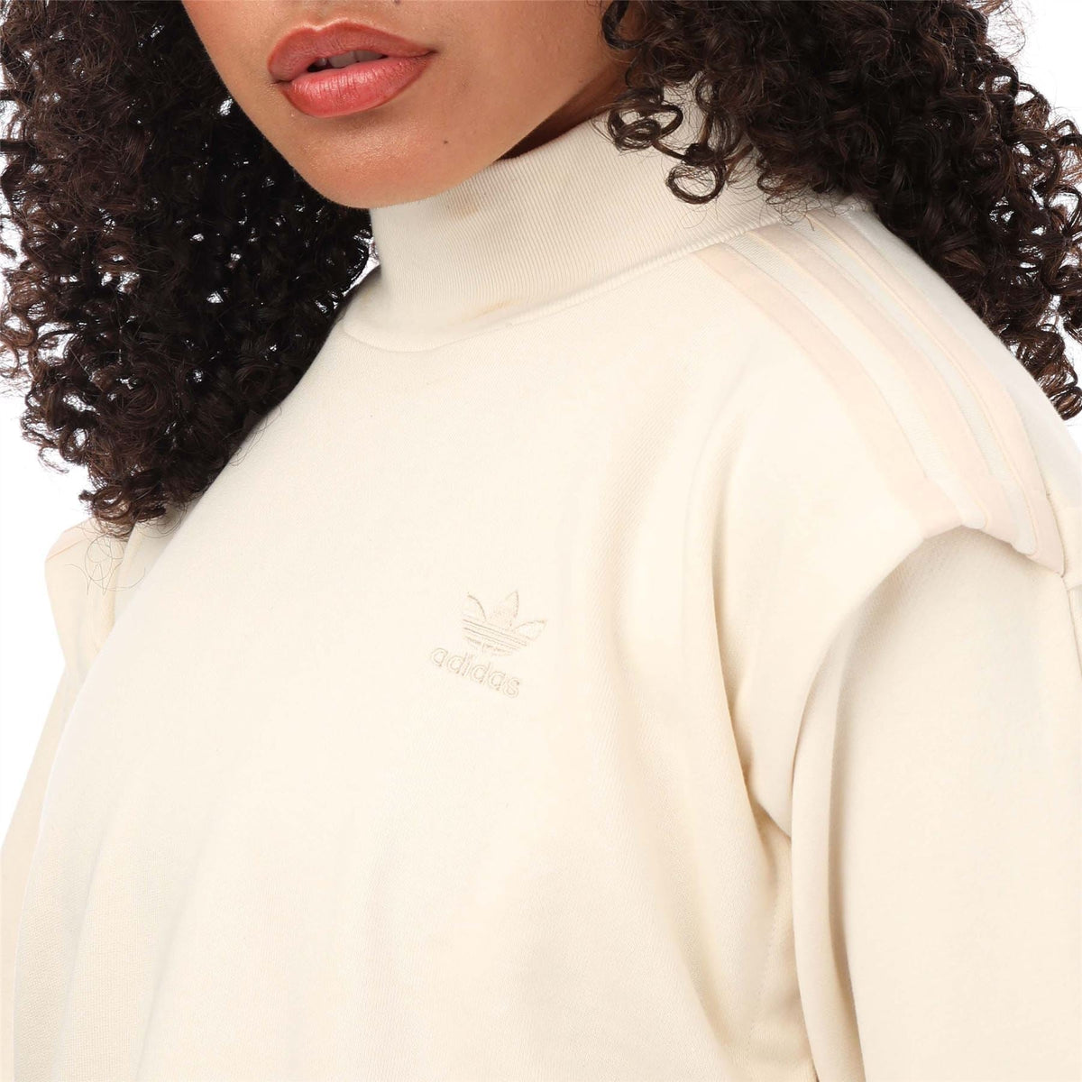 Cream sweatshirt close-up showing adidas Trefoil logo on chest and crewneck collar