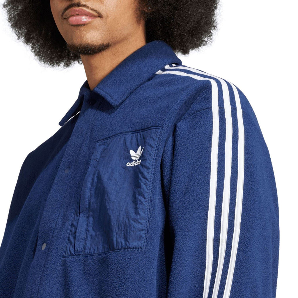 Indigo adidas fleece track shirt close-up with stand collar, chest pocket, and white sleeve stripes