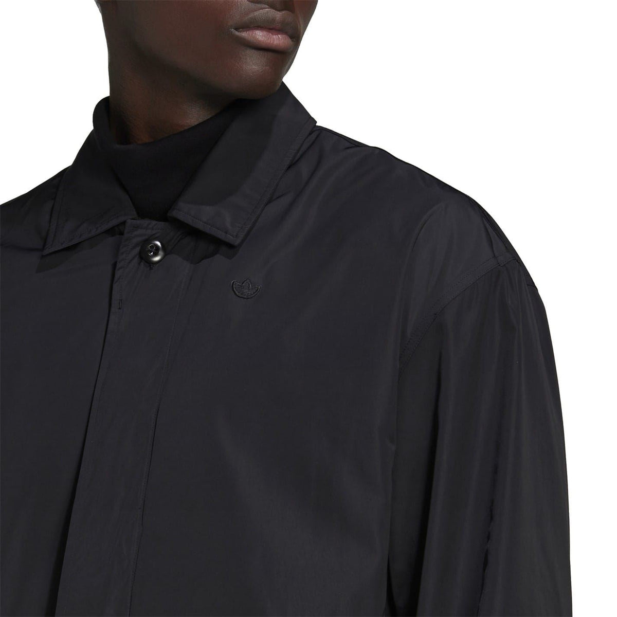 Black stand-collar jacket close-up with button placket and small chest logo.