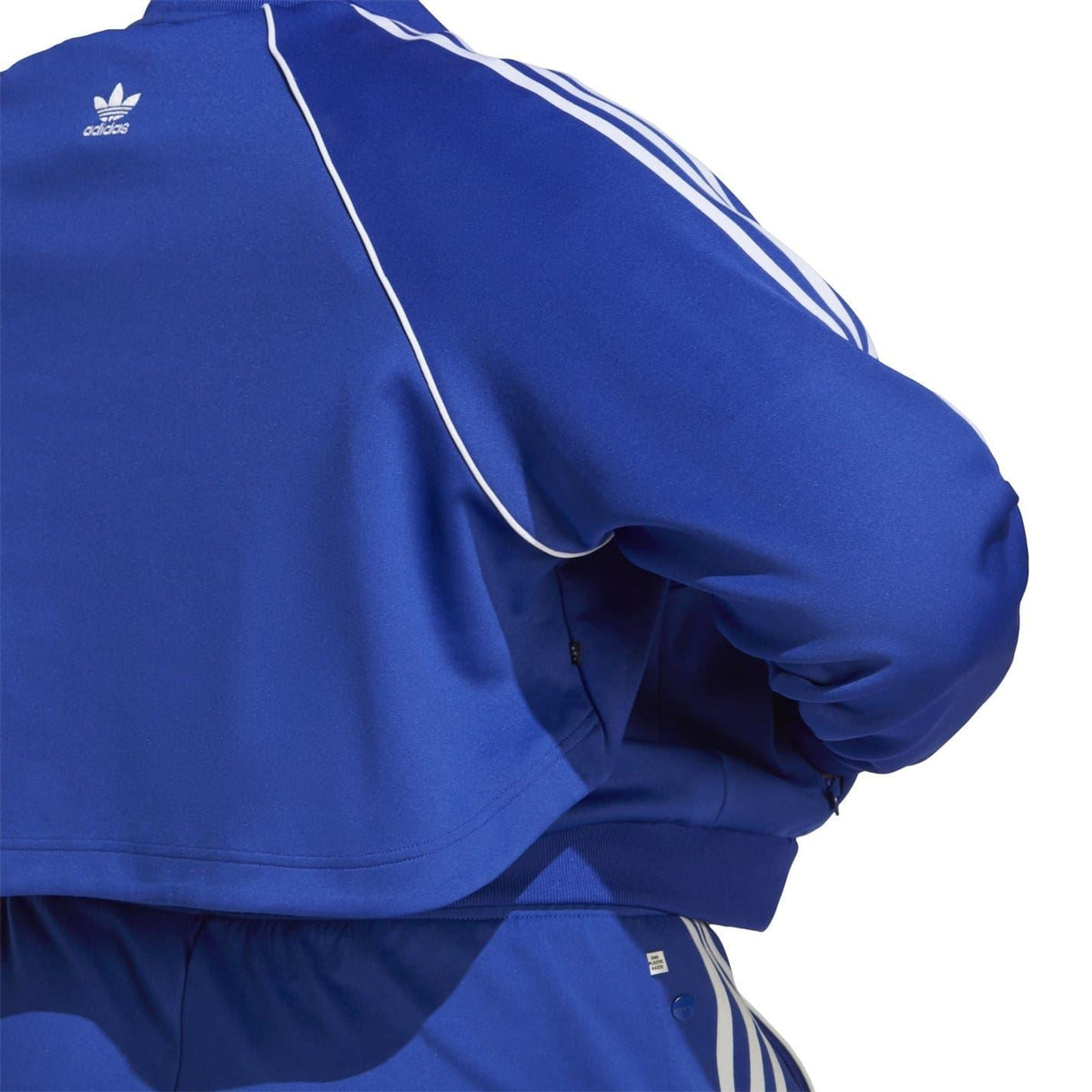 Blue adidas Originals jacket sleeve close-up with white stripe piping and zipper
