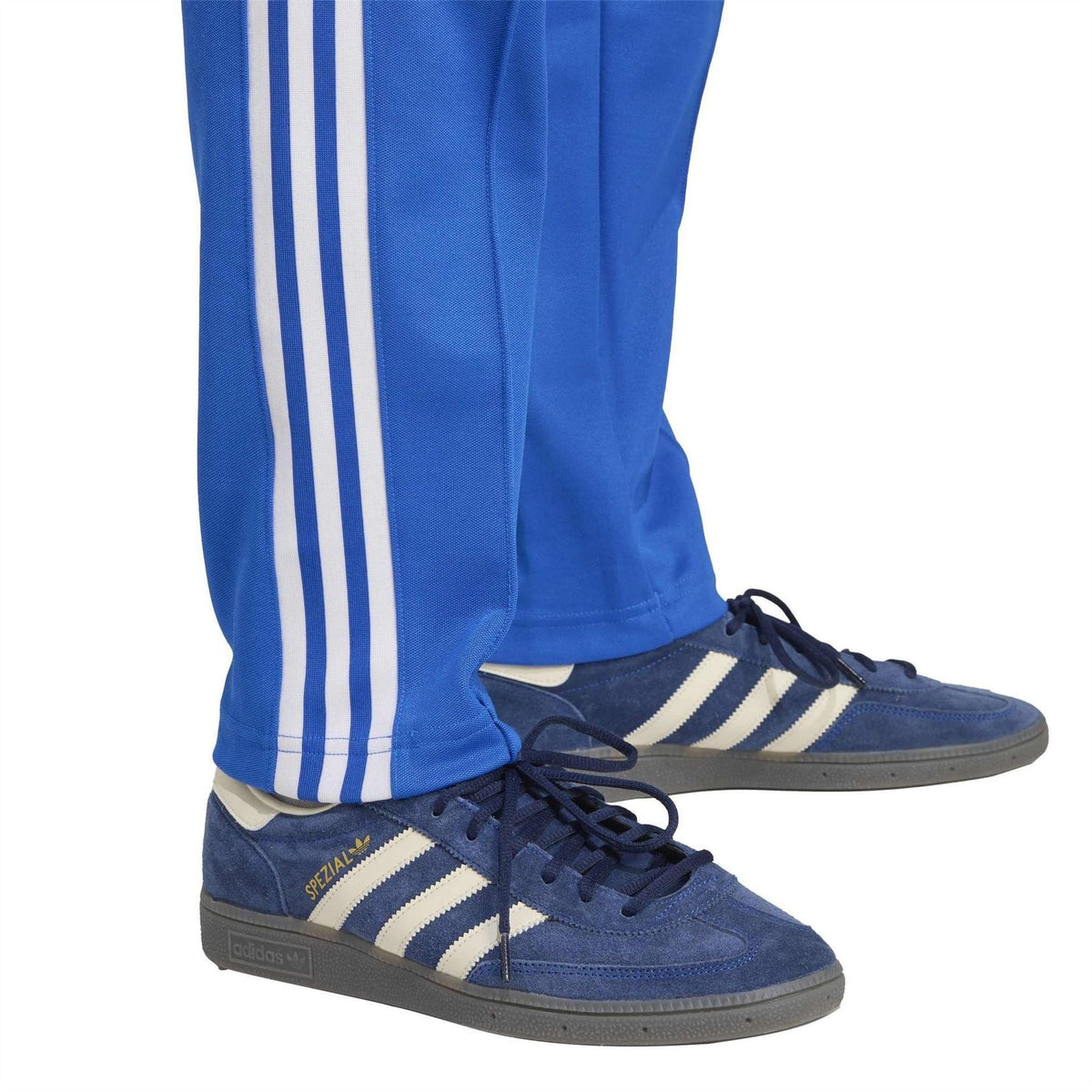Blue adidas track pants with white side stripes and elastic cuffs over sneakers
