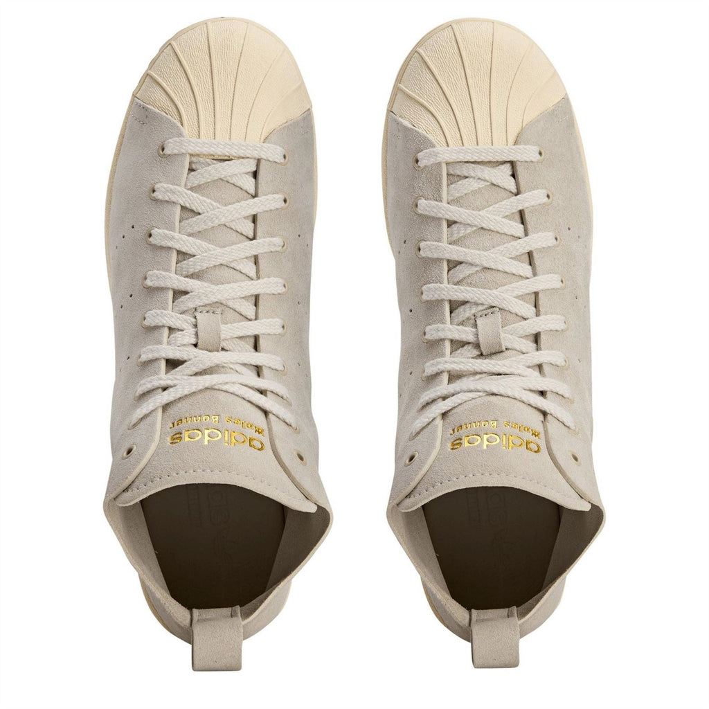 Cream suede sneakers with white laces and adidas logo on tongue, open collar.