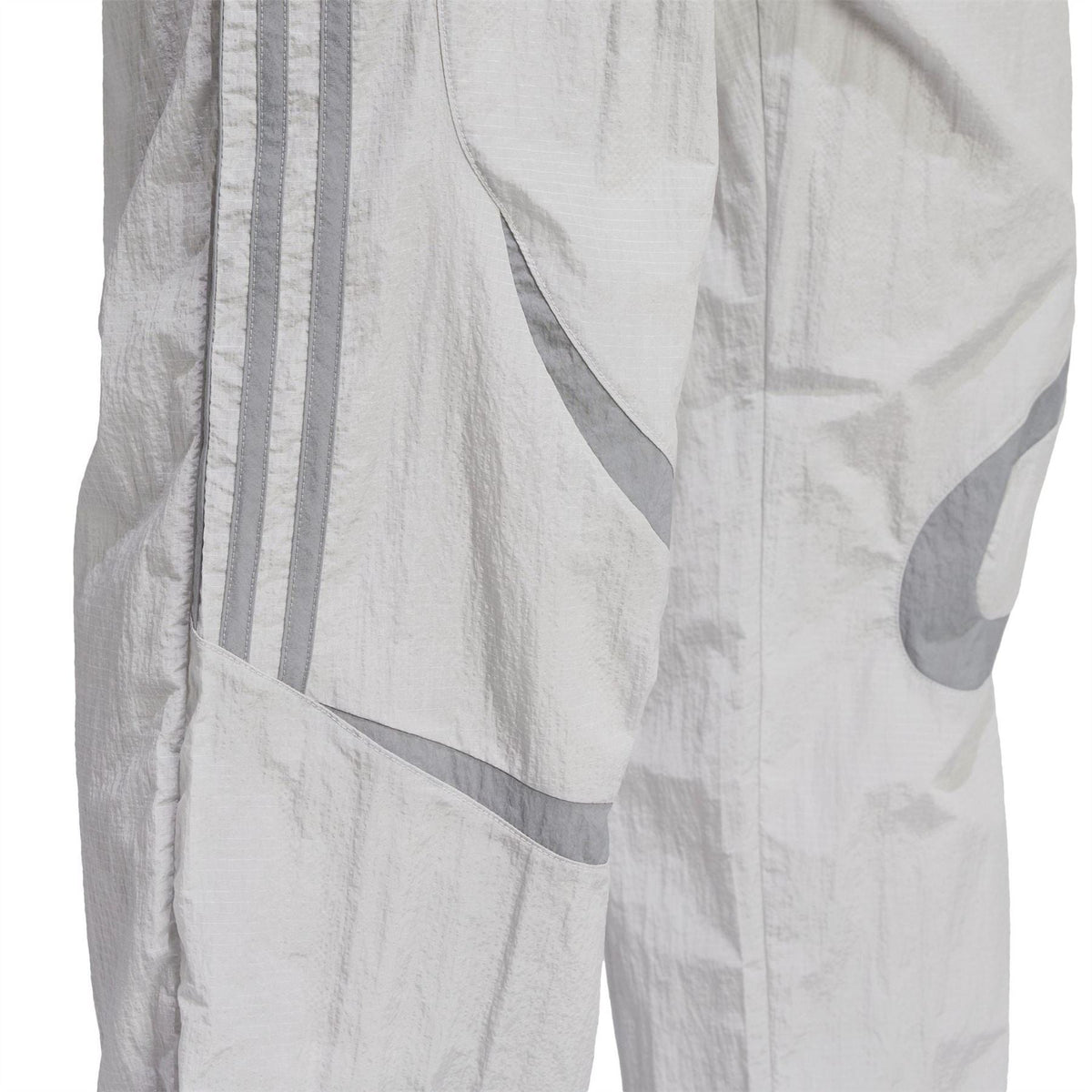 Light grey track pants close-up showing layered panels and adidas logo graphics