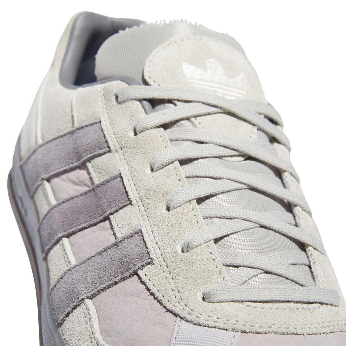 Close-up of beige suede upper with lace-up, purple stripes, and cushioned collar