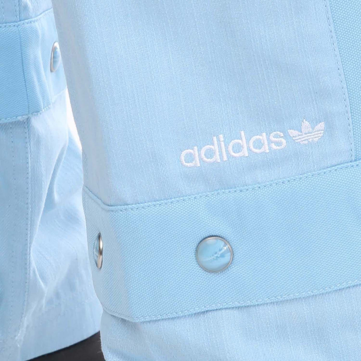 Light blue denim track pants close-up with adidas logo and metal button
