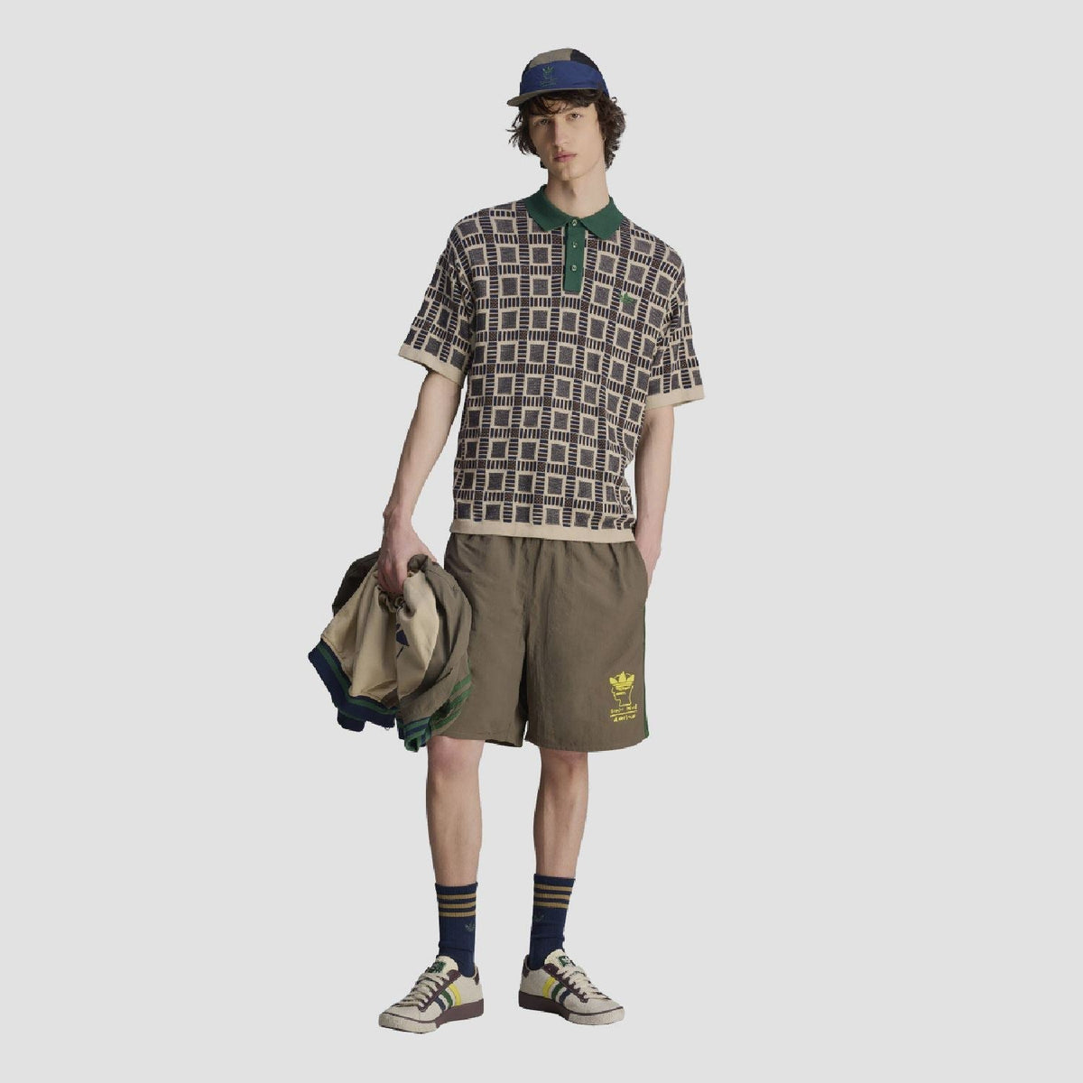 Model wearing sand polo shirt with green collar; navy-and-cream grid pattern with short sleeves.