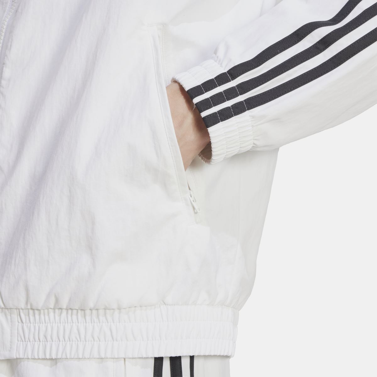 White track jacket close-up of ribbed cuff and black triple-stripe sleeve detail