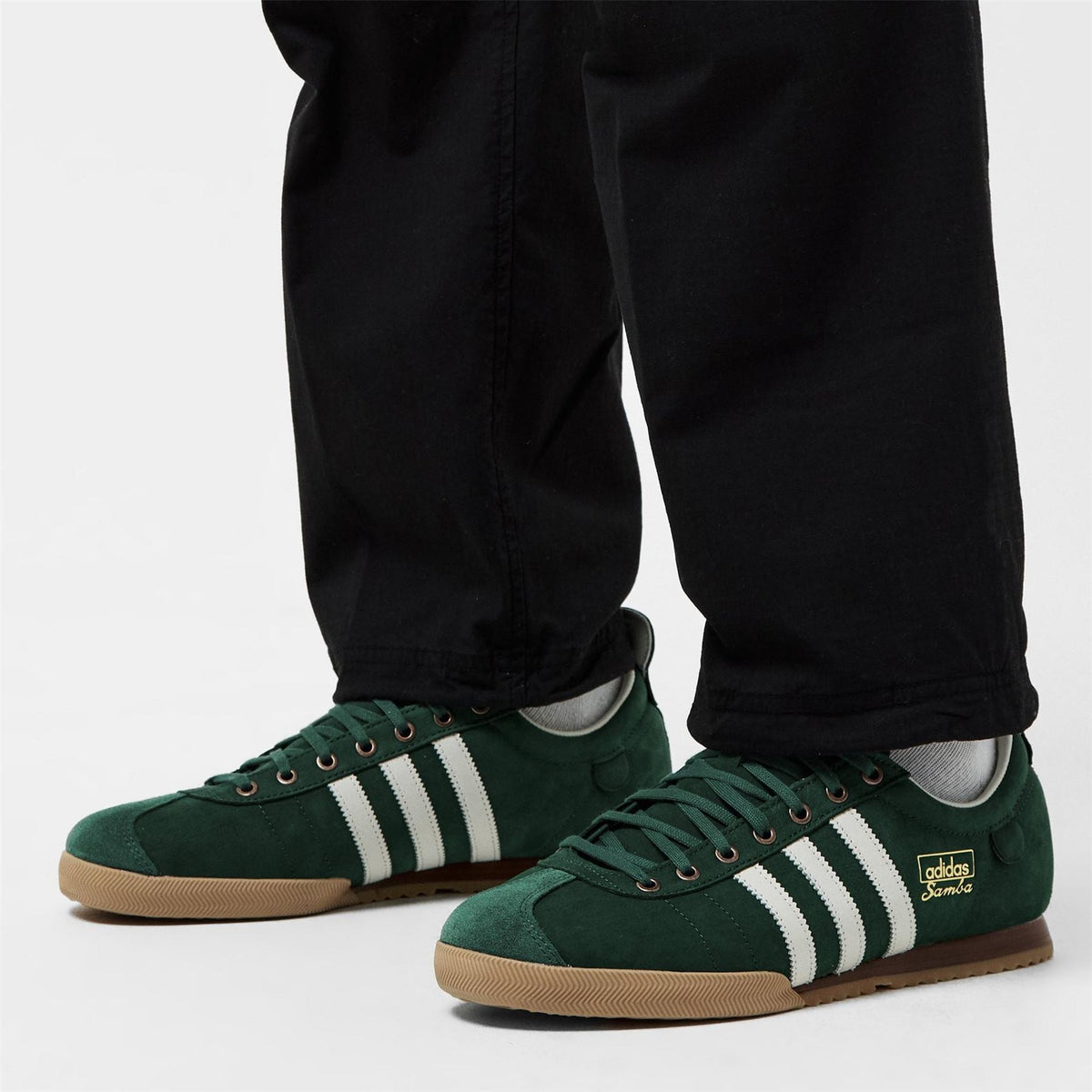 Green Samba low-top sneakers with white stripes, worn with black pants