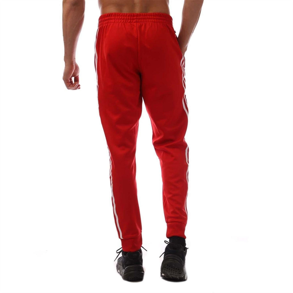 Red adidas SST track pants with white vertical stripes and ribbed ankle cuffs