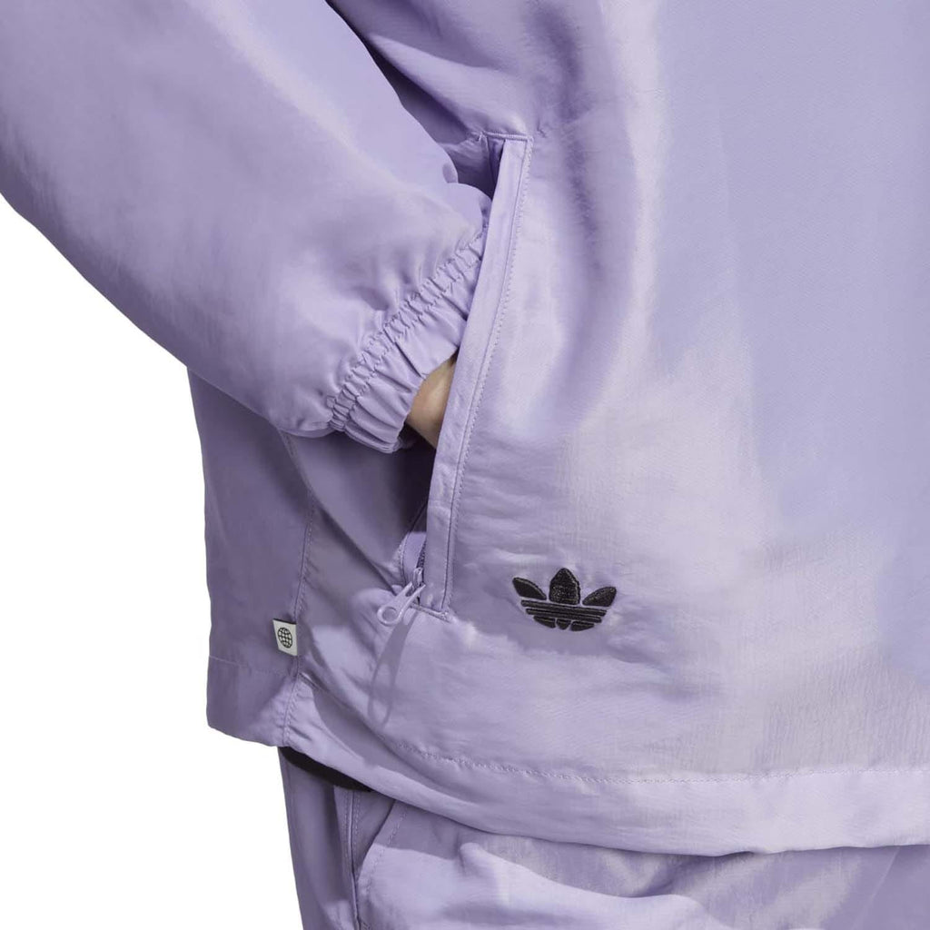 Lilac windbreaker close-up with adidas trefoil logo and zippered pocket detail