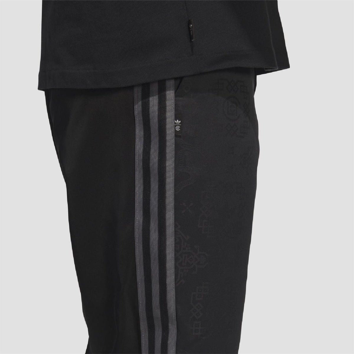 Black track pants close-up: vertical side stripes and textured allover print