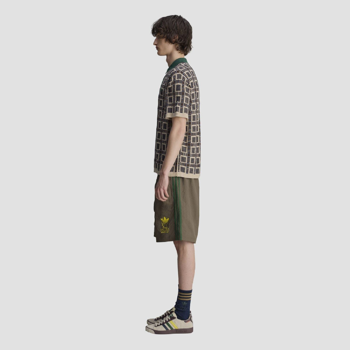 Side view of sand polo shirt; green collar with button placket and navy geometric pattern.