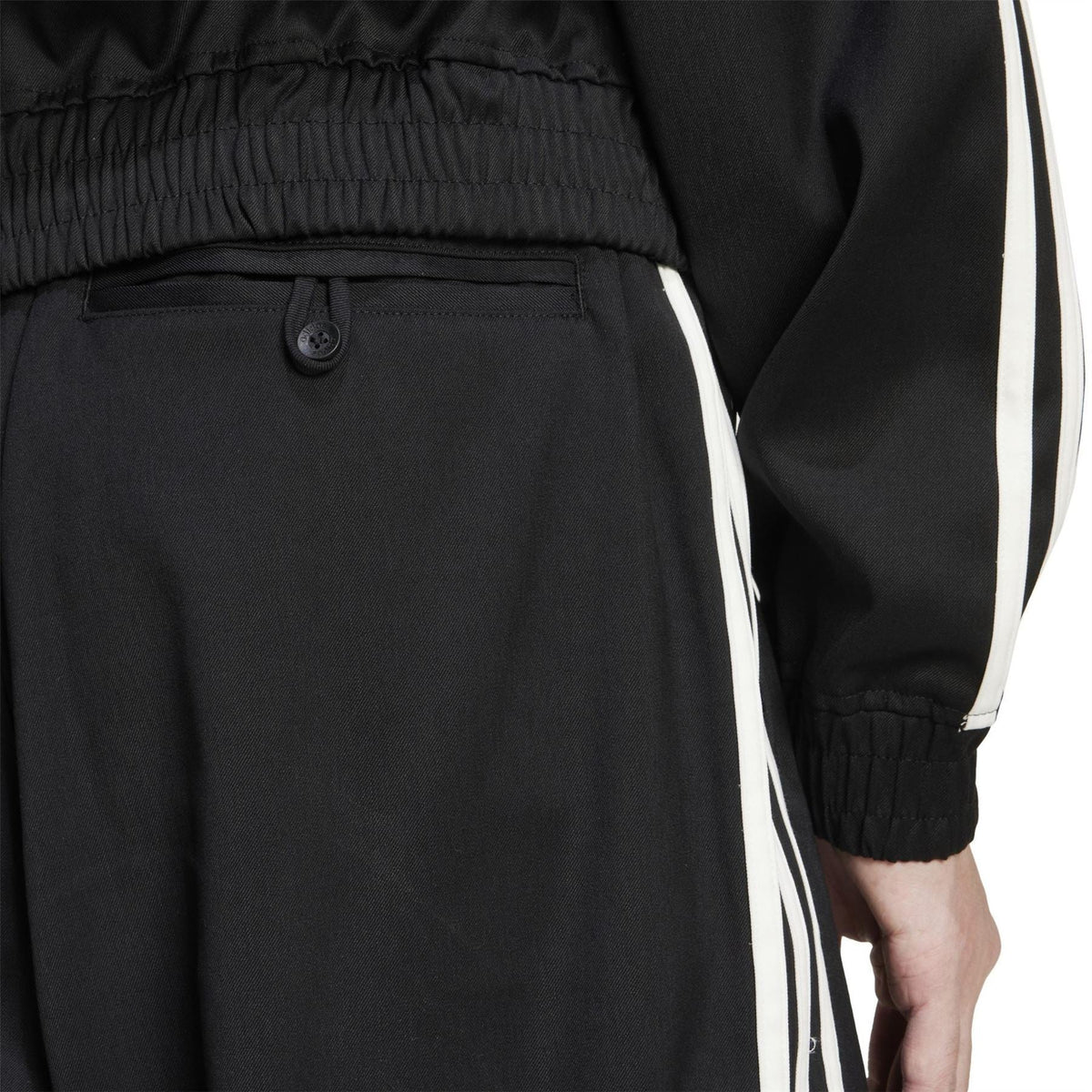 Black track pants close-up: elastic waistband, snap button pocket, side white stripe