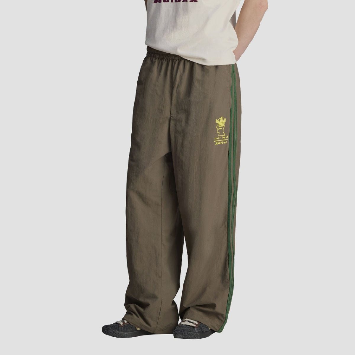 Chocolate track pants with elastic waist, green side stripe, yellow logo patch on leg