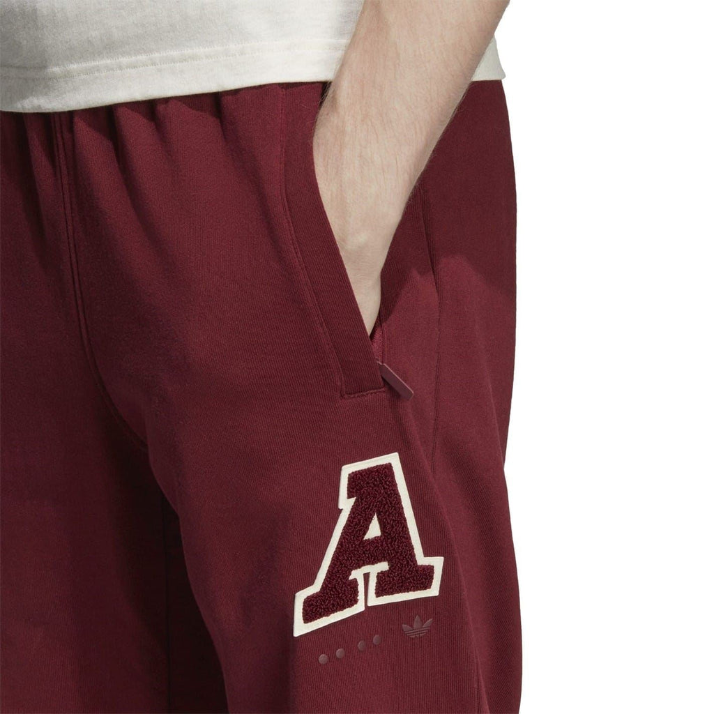 Close-up of burgundy track pants with embroidered A logo on right thigh
