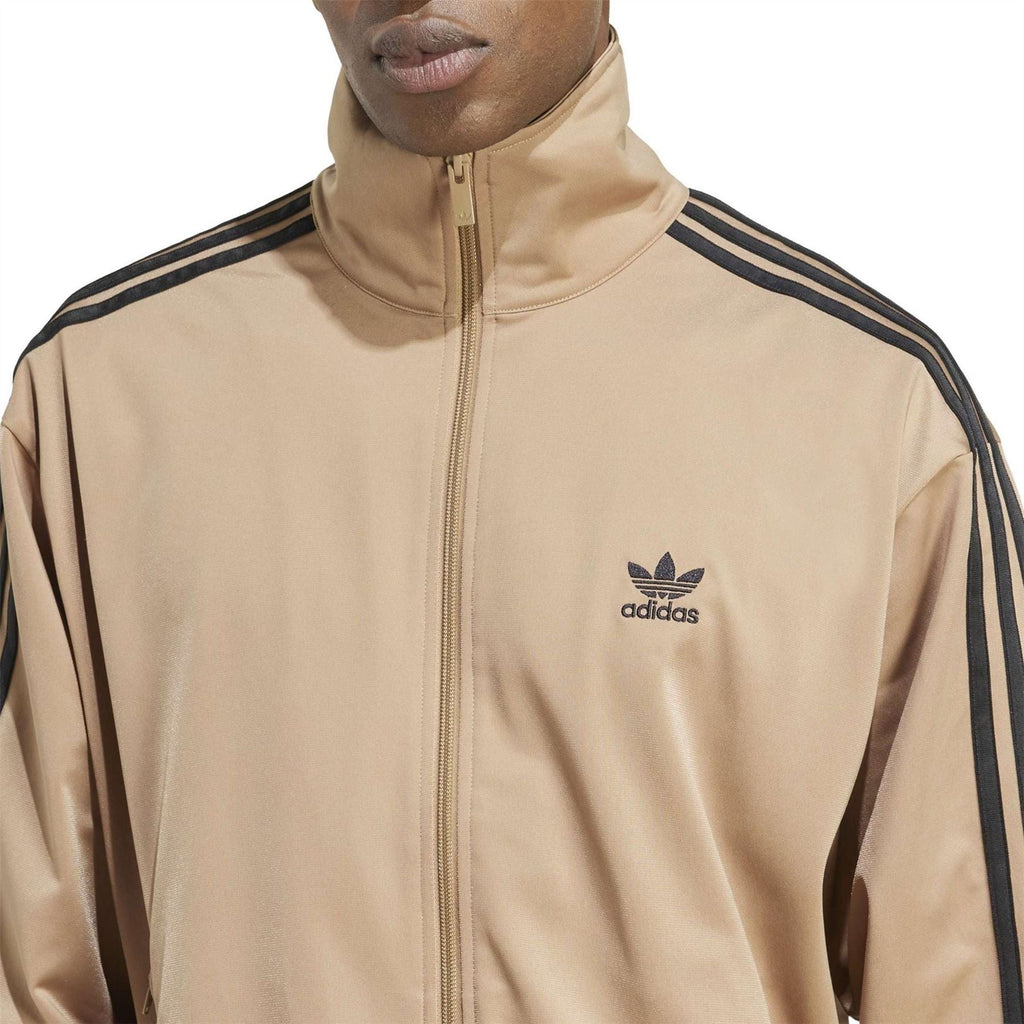 Tan adidas track jacket with zip front, adidas logo, and black triple-stripe sleeve detail.