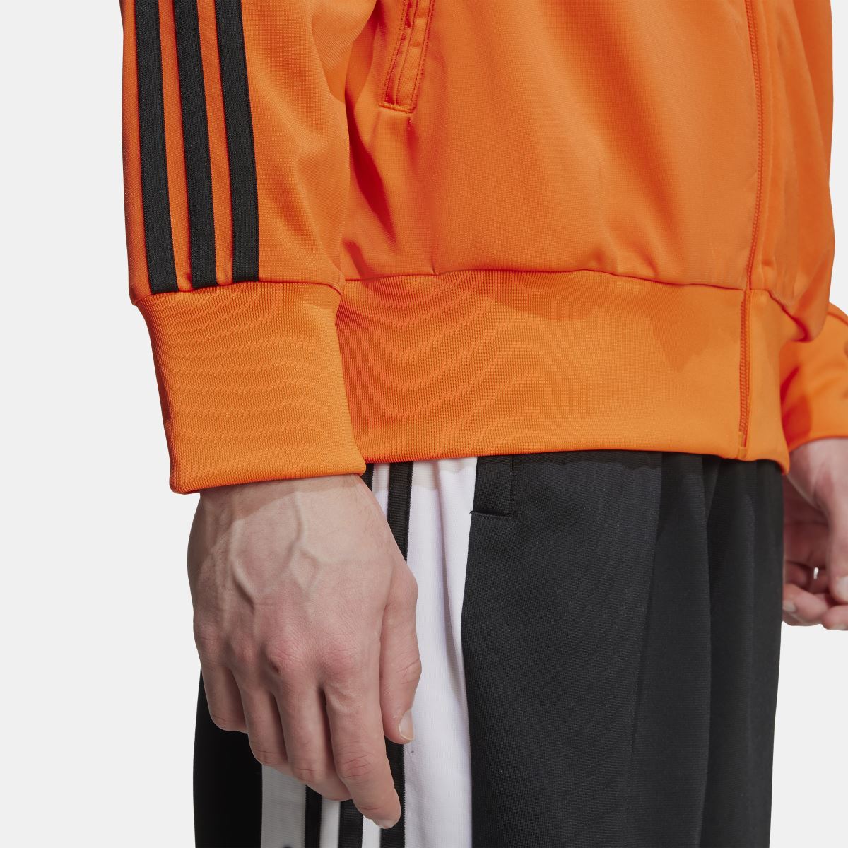adidas Originals Adicolor Classics Firebird Track Top in vibrant red with white stripes, shown on a hanger against a white background.