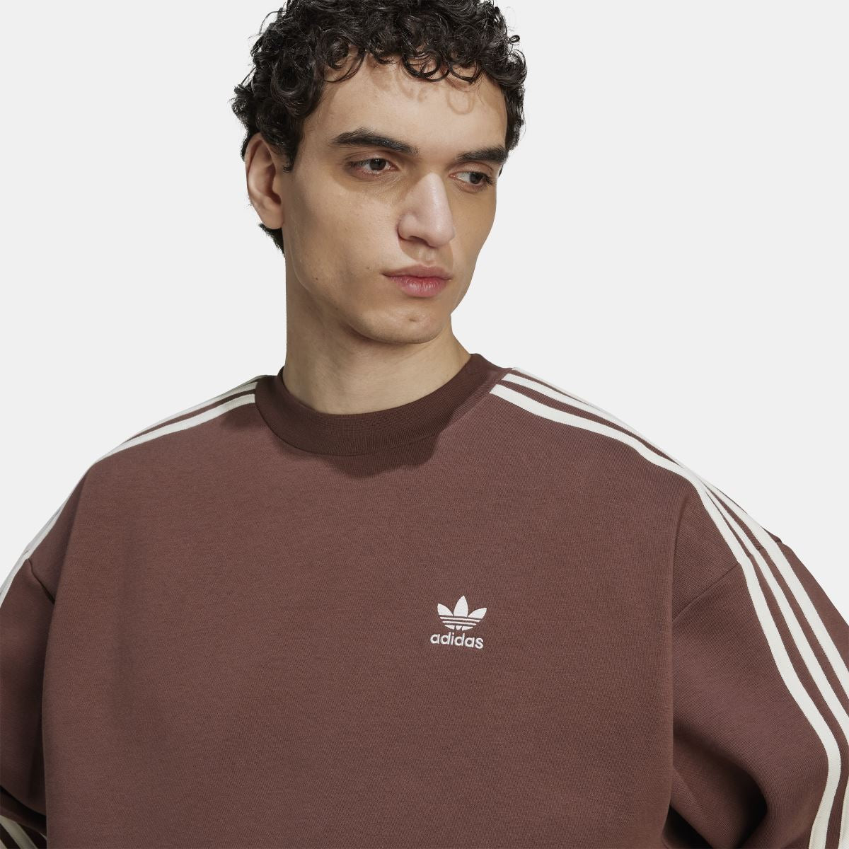 Brown crewneck sweatshirt close-up: Adidas trefoil logo and shoulder sleeve stripes