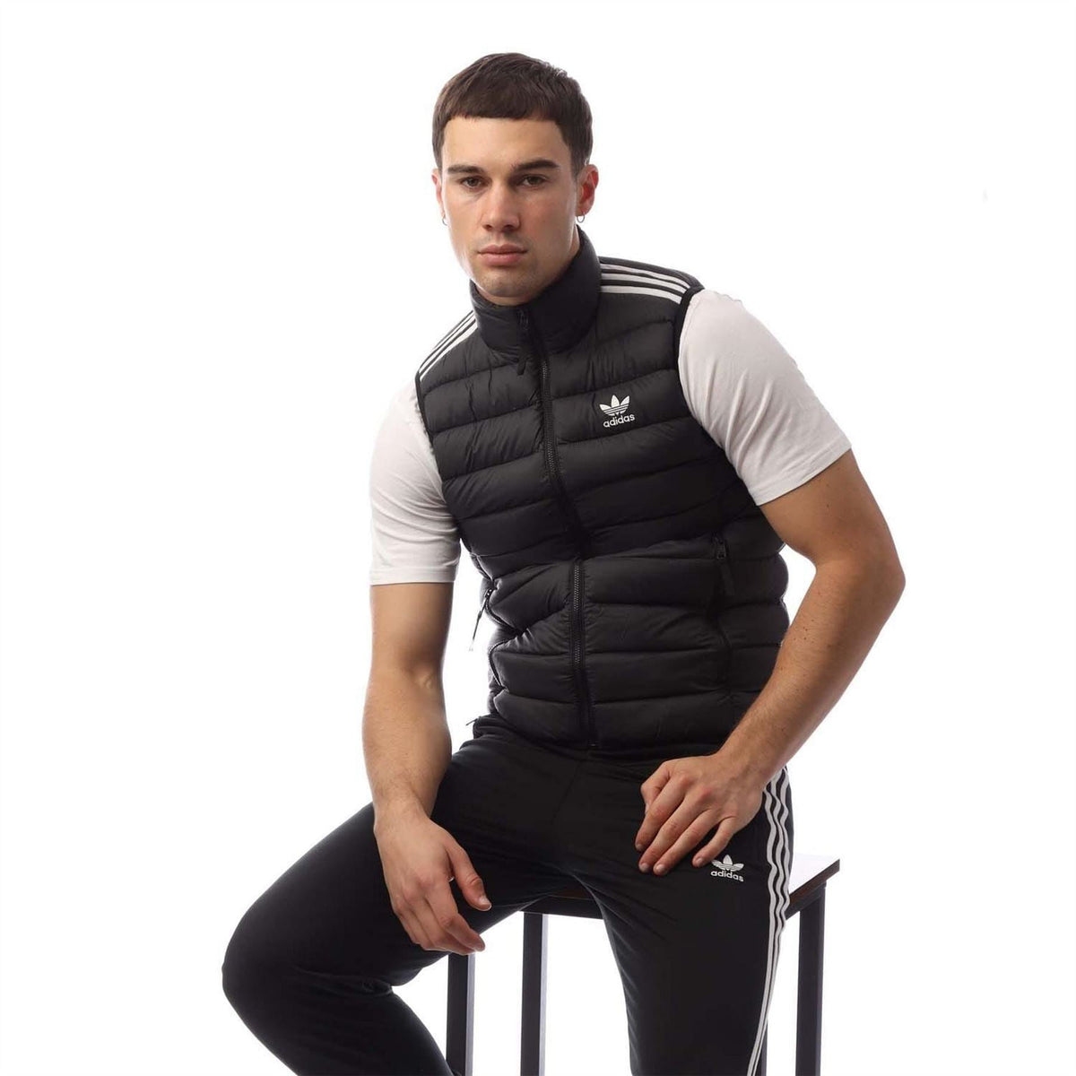 Black puffer vest with stand collar and zip front, adidas trefoil and shoulder stripes.