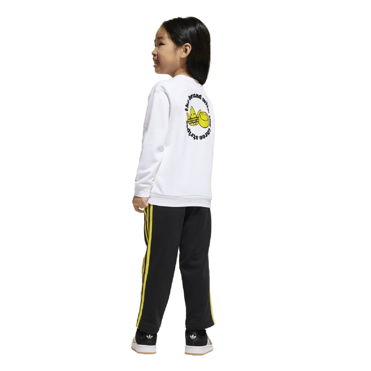 Kids white sweatshirt with back Smiley text graphic and black joggers with yellow side stripes.