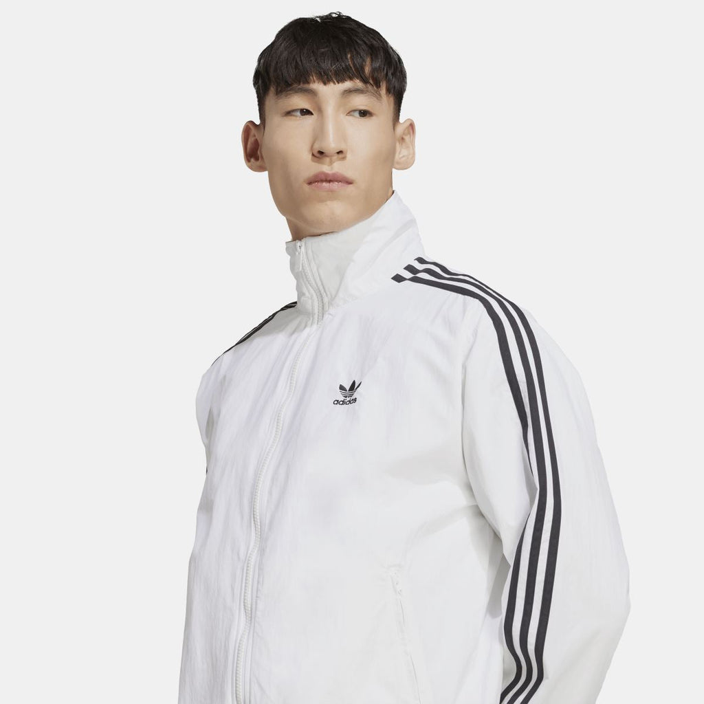 White track jacket close-up with adidas trefoil logo and black triple-stripe shoulder detail