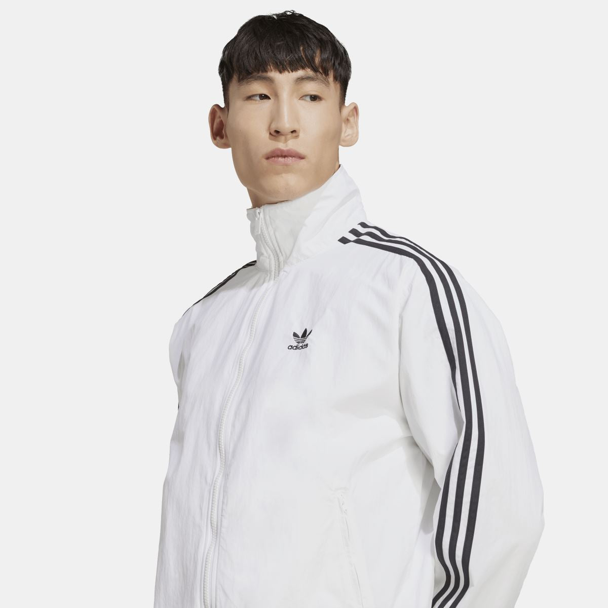 White track jacket close-up with adidas trefoil logo and black triple-stripe shoulder detail