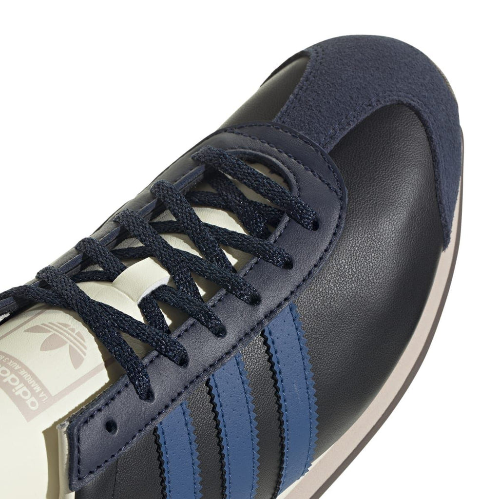 Close-up of navy/black lace-up upper with blue stripe overlays and cream tongue branding