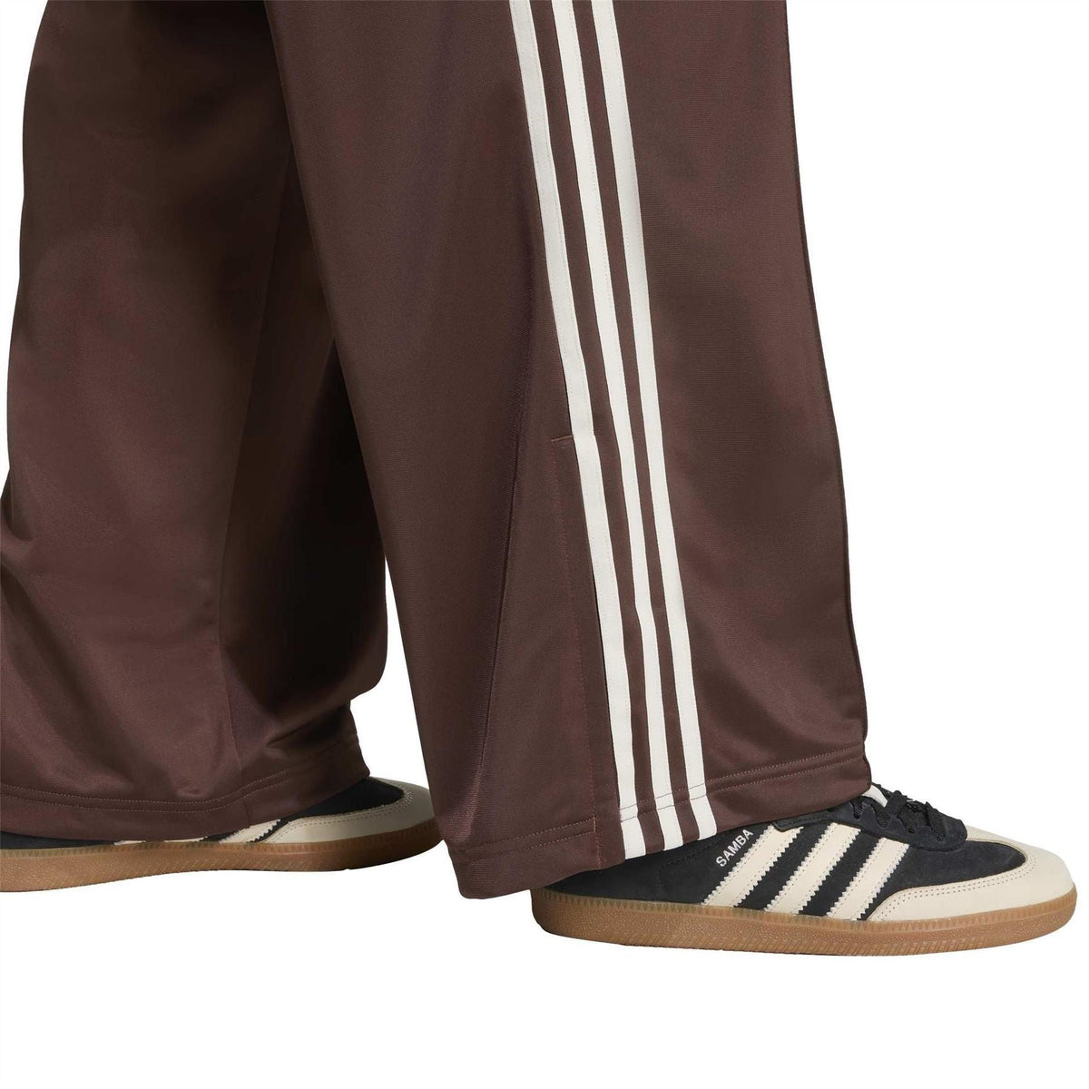Brown adidas track pants with white side stripes and relaxed tapered cuff