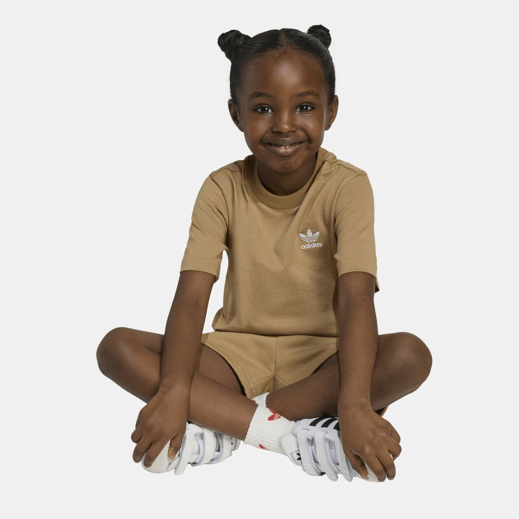 Tan adidas juniors T-shirt and shorts set on model, seated; matching hem and leg logos