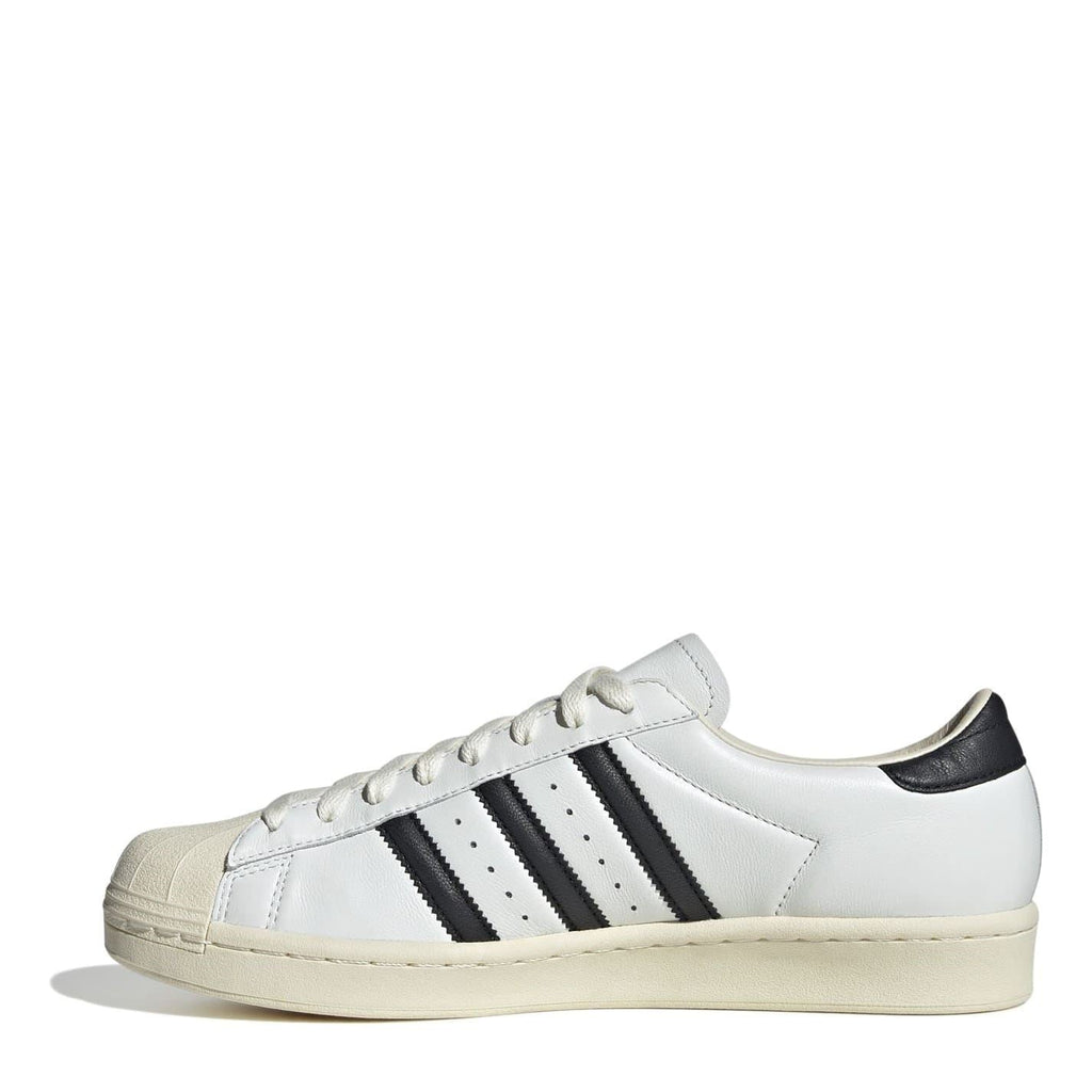White low-top sneakers with black side stripes, lace-up, beige sole
