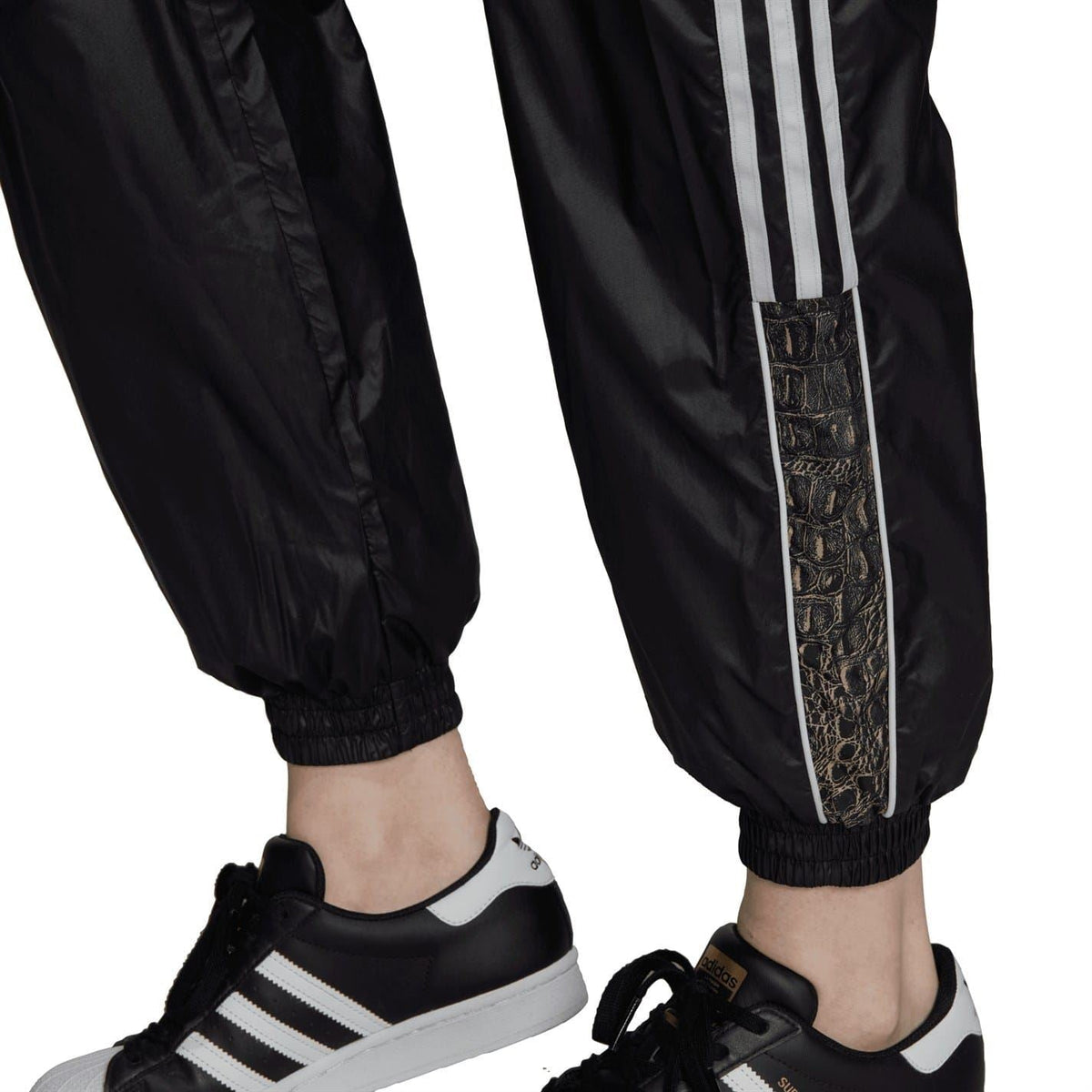 Black track sweatpants with white side stripes and ribbed ankle cuffs, worn with sneakers