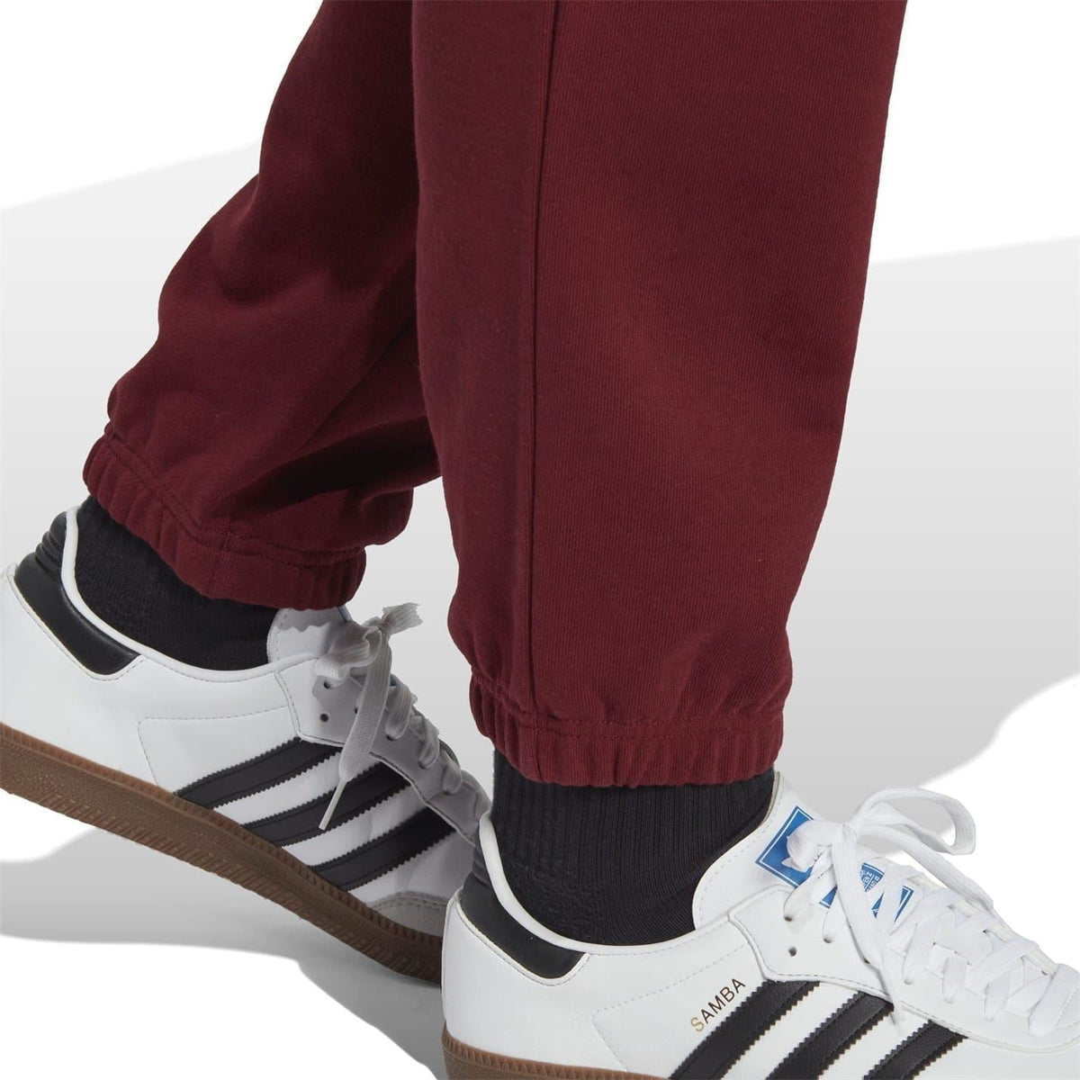 Burgundy track pants with cuffed hem and side pocket; white sneakers shown