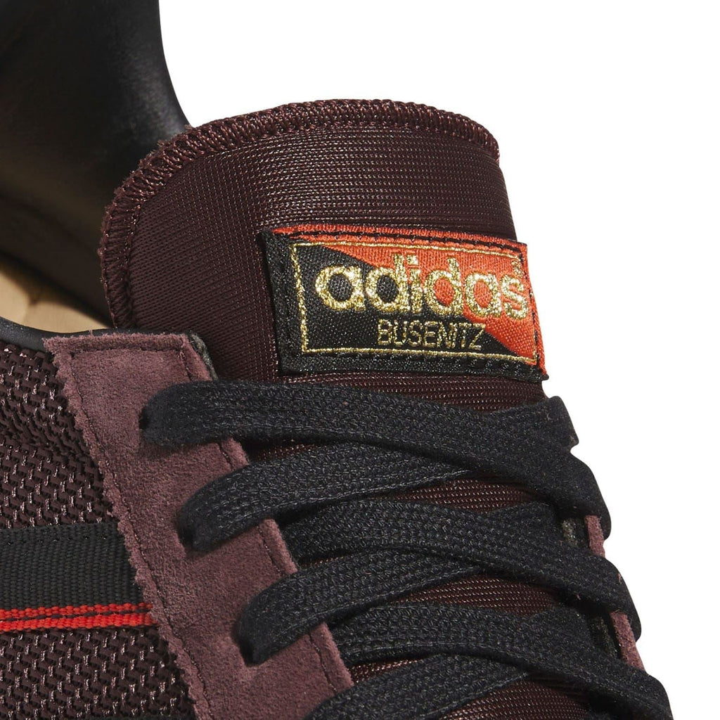 Close-up of brown tongue label and black laces on low-top trainers with red-striped branding