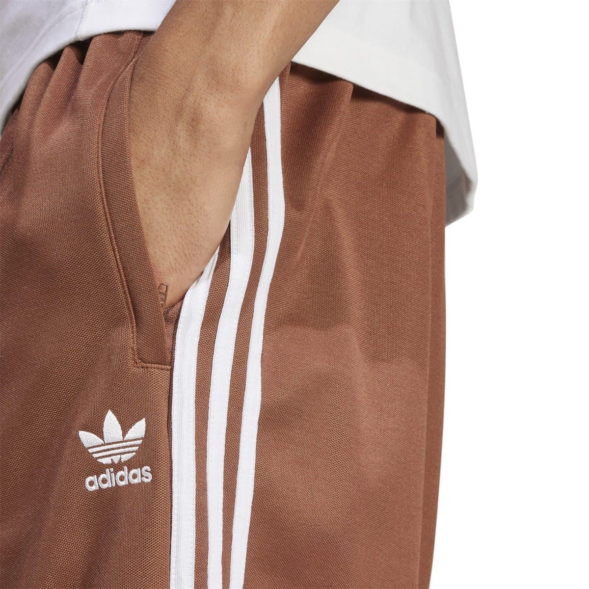 Brown track pants close-up: adidas logo and white triple side stripes