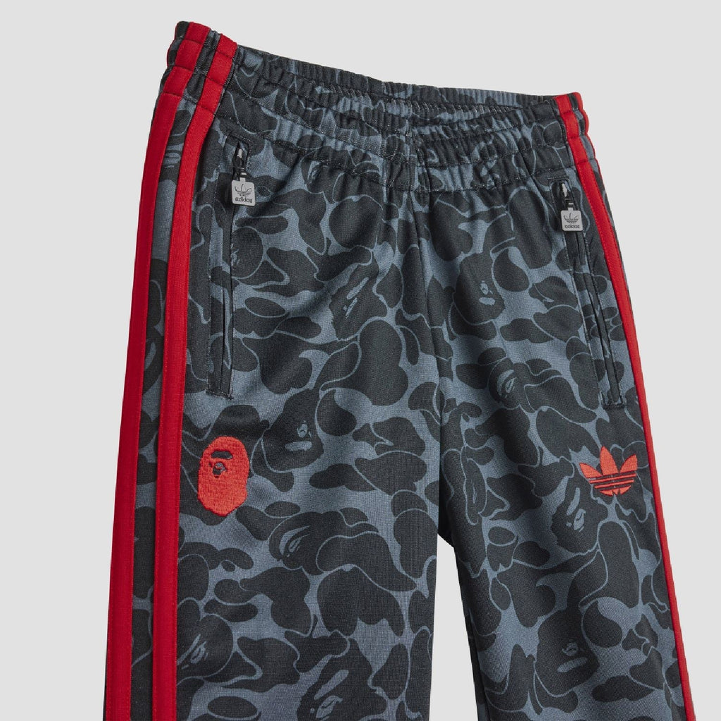 Kids camo track pants with drawstring waist, red side stripes, and red logo patch