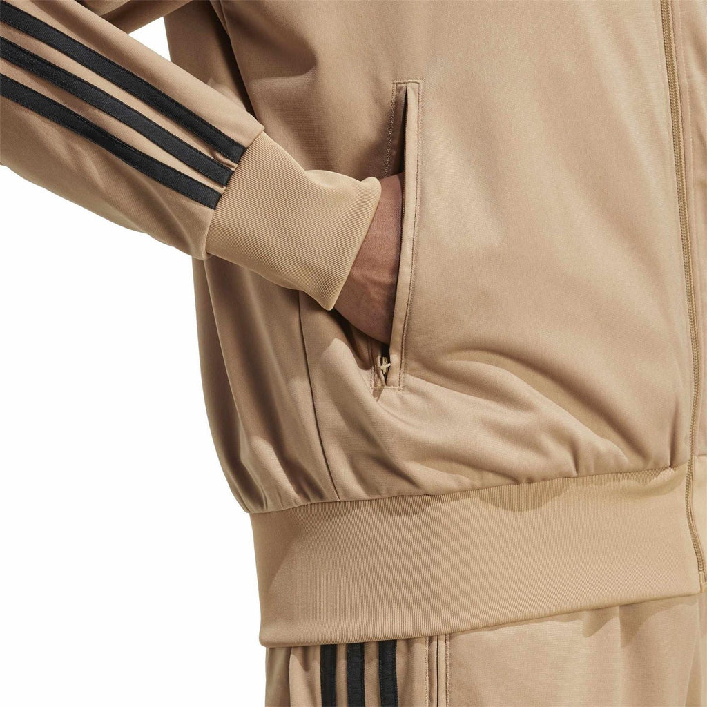 Tan track jacket close-up of zip pocket and ribbed hem with black stripe detail.