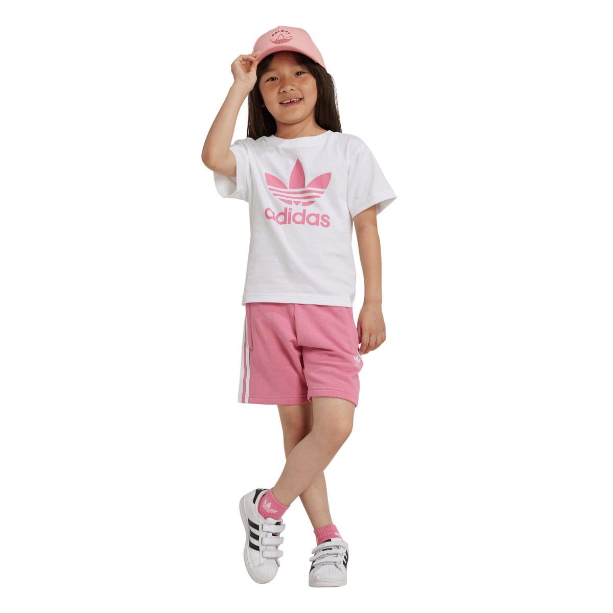 Girl in kids adidas set with pink cap: white T-shirt and pink shorts