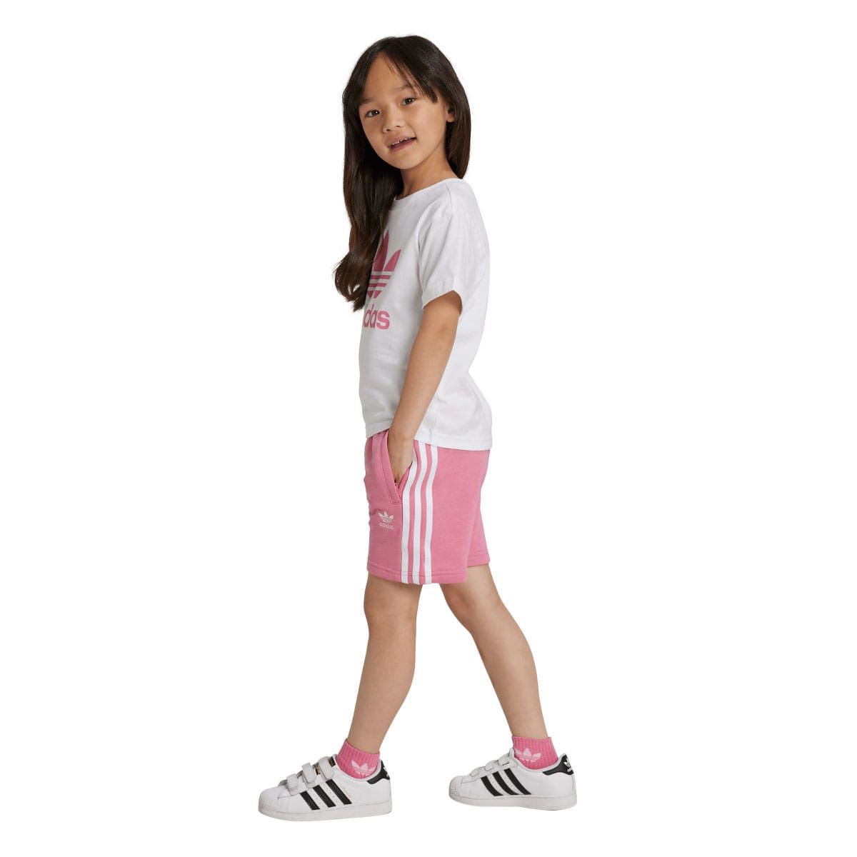Girl modeling kids adidas set from the side: white T-shirt and pink shorts