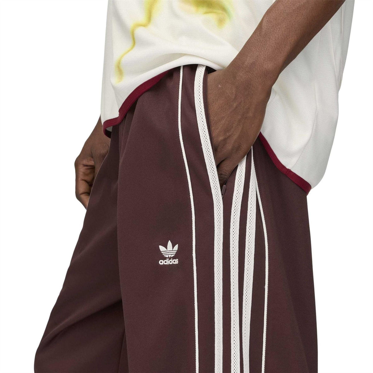 Dark maroon track pants close-up with adidas trefoil logo and white vertical stripe detail.