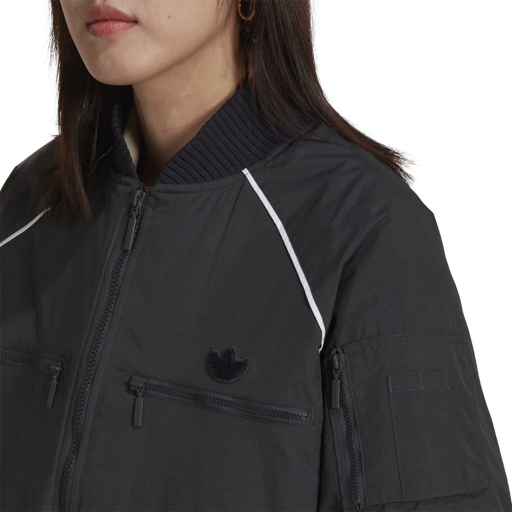 Dark bomber jacket close-up: stand collar, front zipper, flap pockets, small logo.