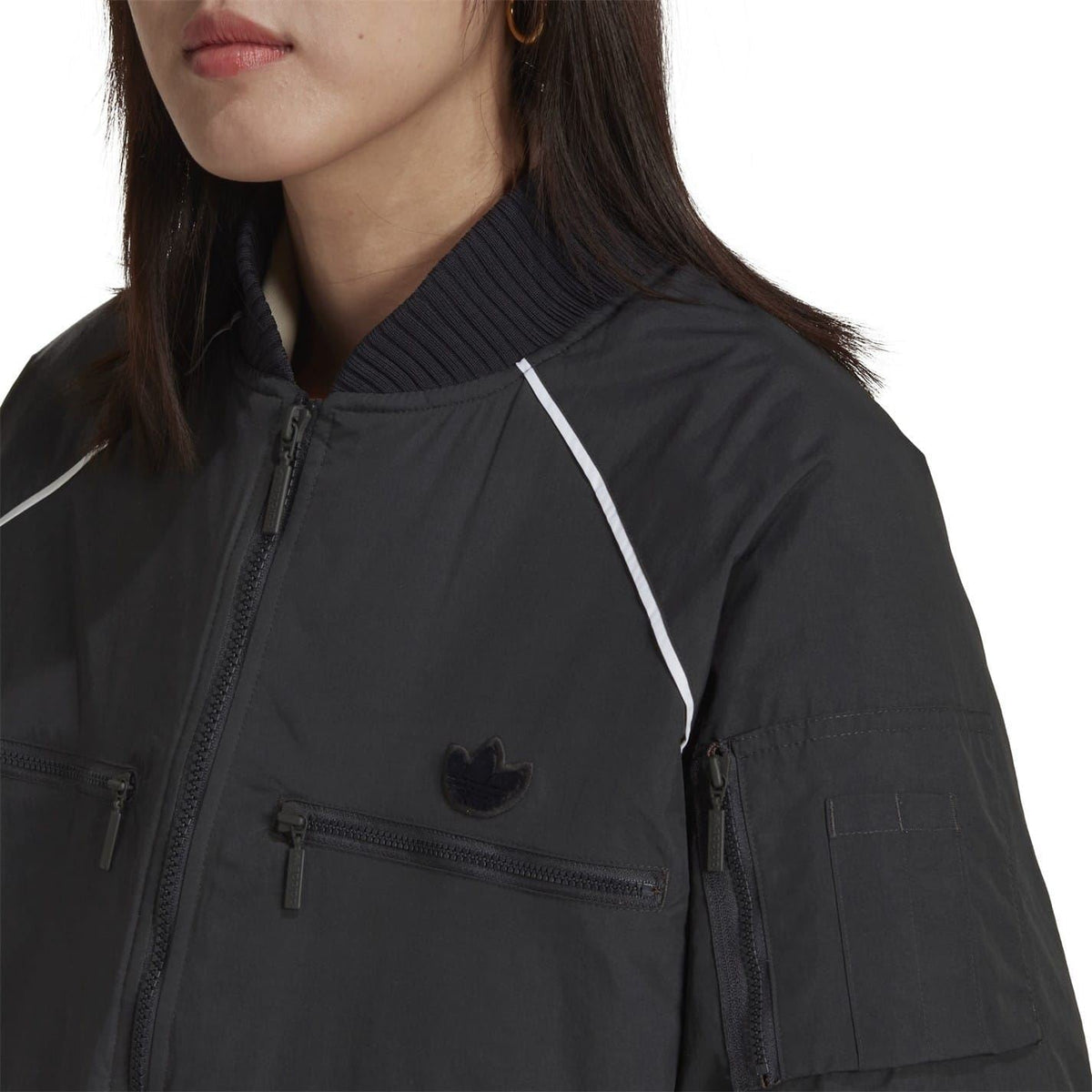 Dark bomber jacket close-up: stand collar, front zipper, flap pockets, small logo.