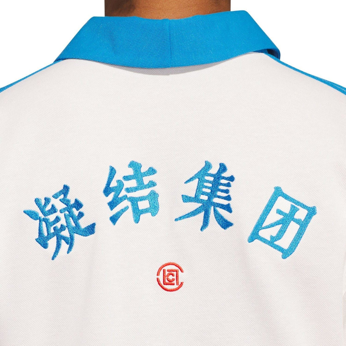 Back of white polo shirt showing blue graphic text and small red emblem near collar.