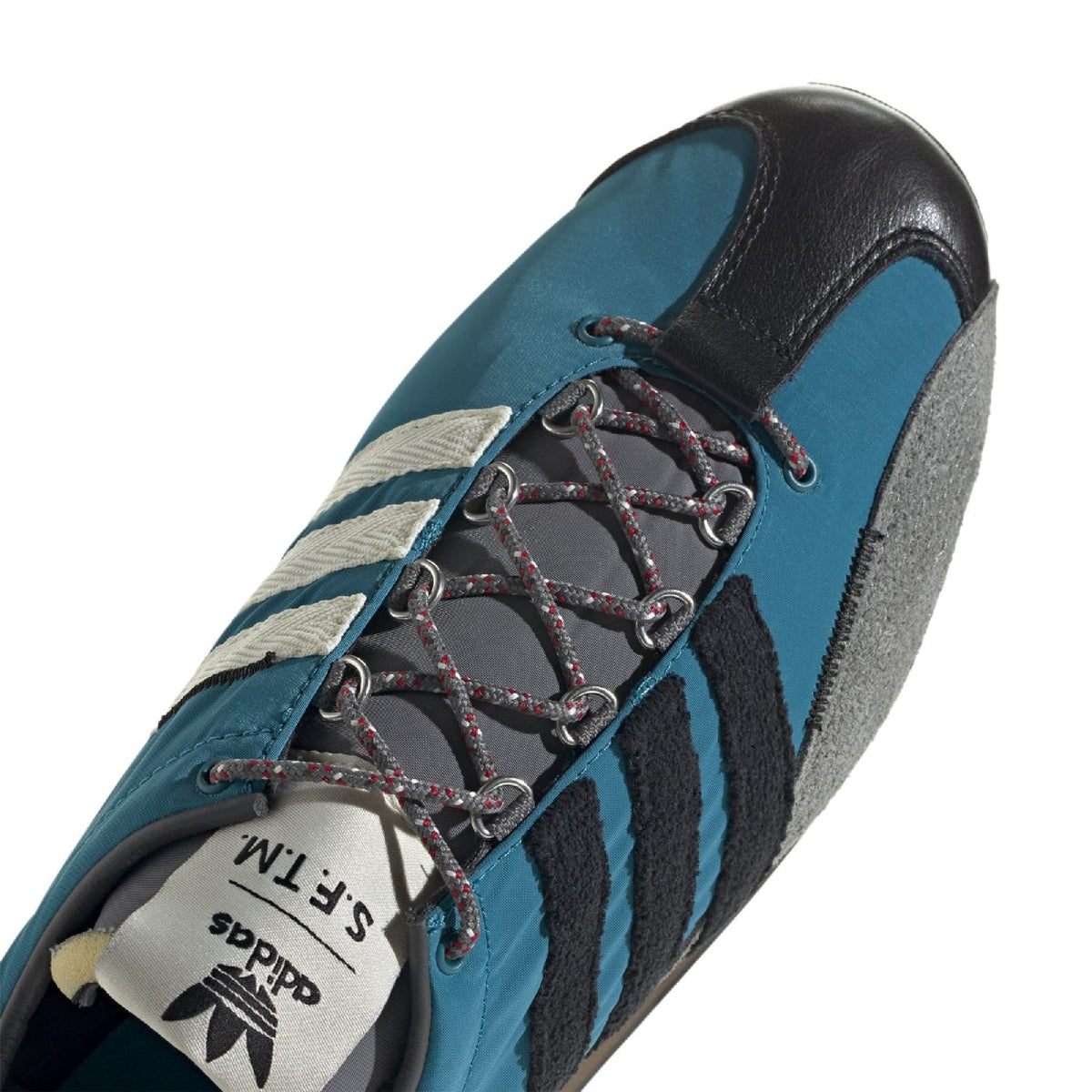 Close-up of teal trainer upper with black overlay, gray panel and lace hooks detail