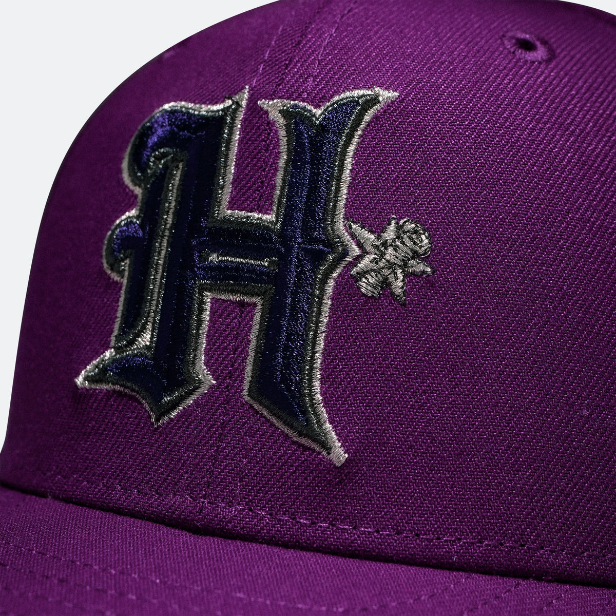 Close-up of embroidered H logo on a purple baseball cap